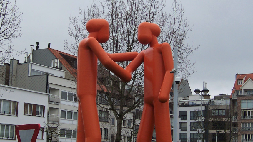 Image shows giant plastic sculpture of two abstract humans shaking hands.